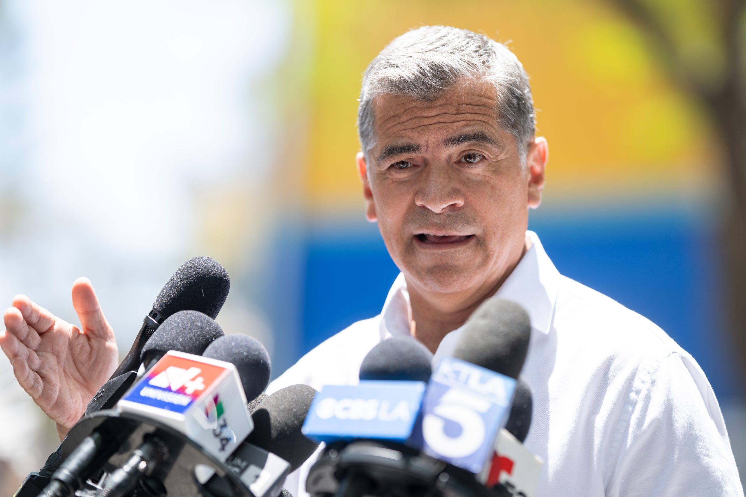A photo of former HHS Secretary Xavier Becerra speaking in front of news reporters' microphones.