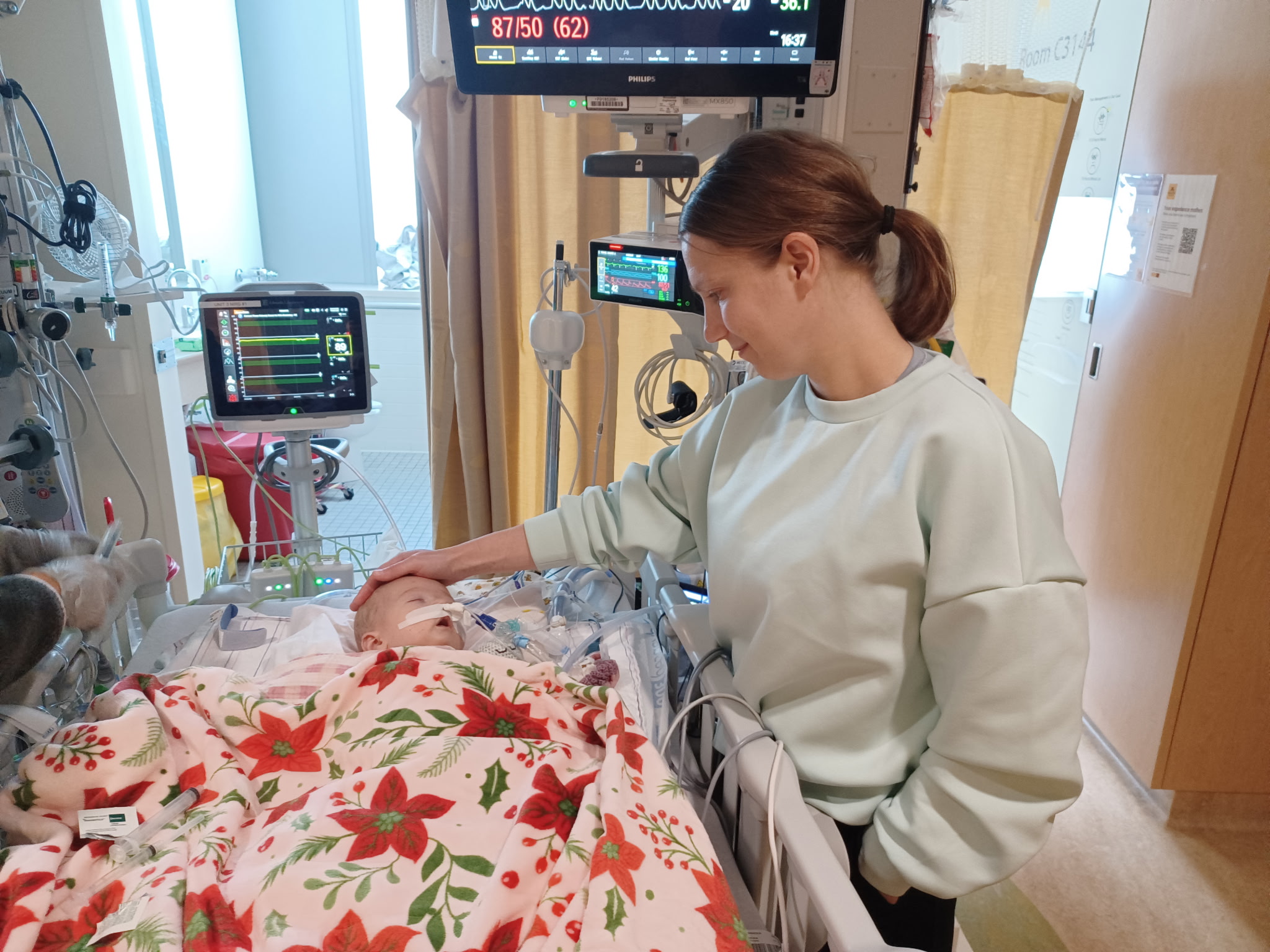 Betsy Adler pets her daughter's forehead. Her daughter is in a hospital bed.