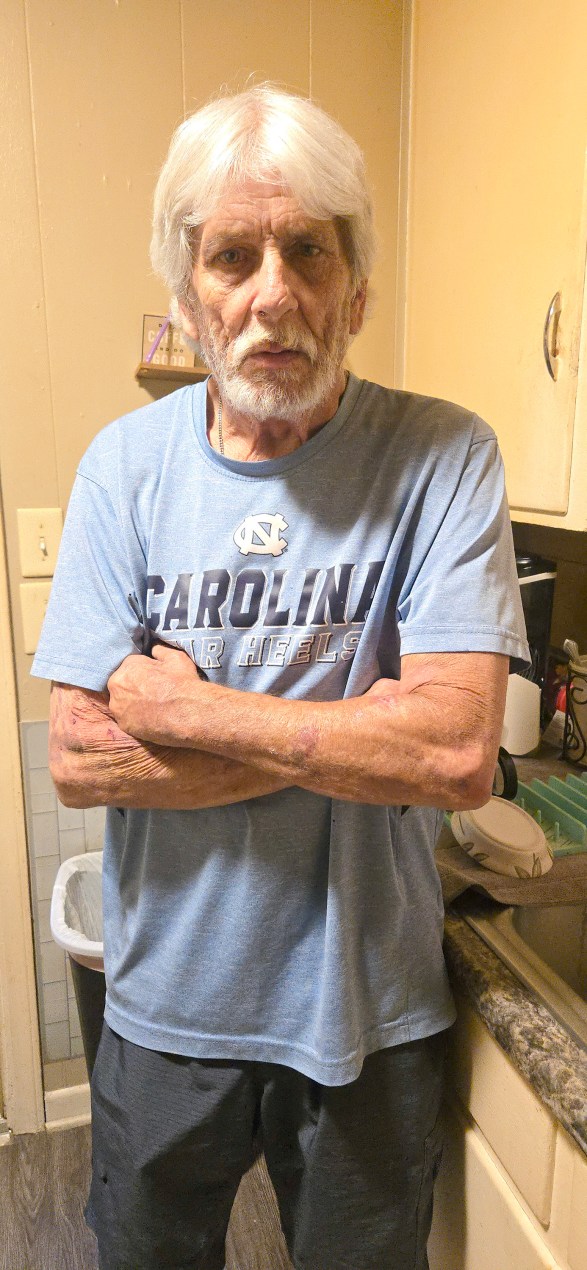 An older man with white hair stands with his arms crossed.